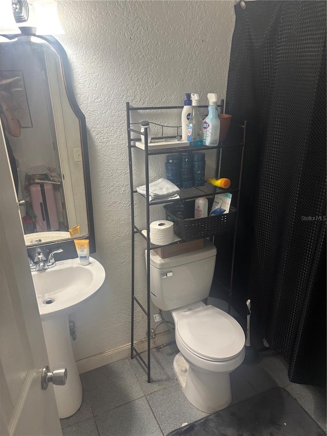 bathroom with a textured wall, toilet, and baseboards