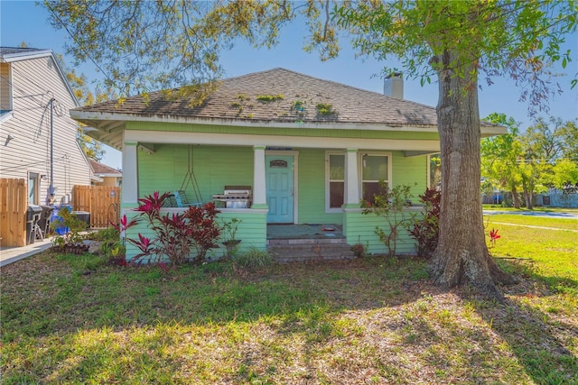 bungalow-style home with a front lawn, a porch, fence, roof with shingles, and a chimney