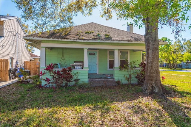 bungalow with a front lawn, a porch, fence, roof with shingles, and a chimney