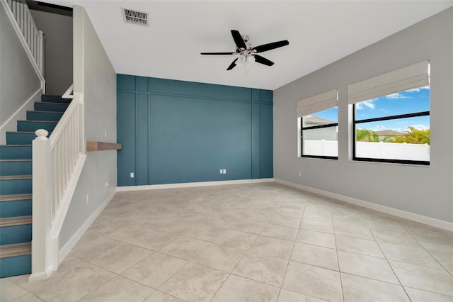 unfurnished room with ceiling fan, light tile patterned floors, visible vents, baseboards, and stairway