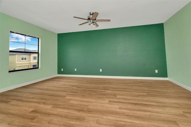 empty room featuring ceiling fan, an accent wall, wood finished floors, and baseboards