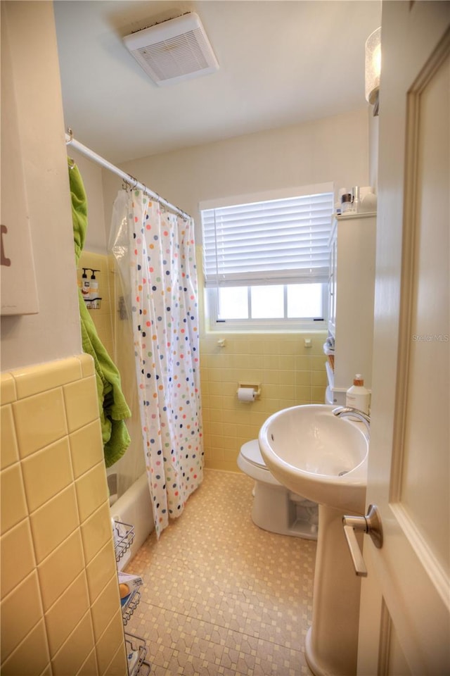 bathroom with tile walls, visible vents, toilet, a sink, and tile patterned floors