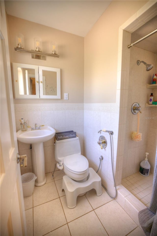 bathroom with tiled shower, toilet, a sink, tile patterned flooring, and tile walls