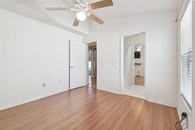 unfurnished bedroom with light wood-type flooring, multiple windows, lofted ceiling, and baseboards