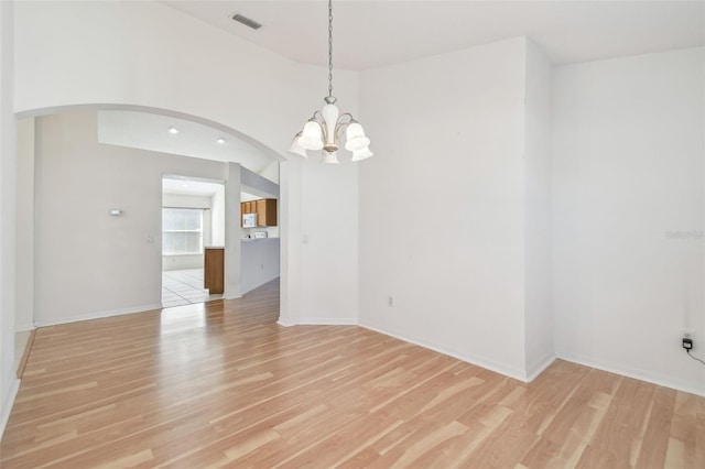 spare room featuring arched walkways, baseboards, visible vents, and light wood-style floors