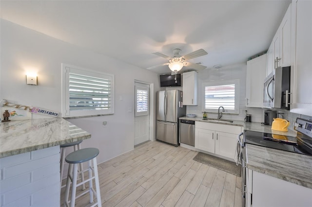 kitchen with light stone countertops, light wood-style flooring, white cabinets, stainless steel appliances, and a sink