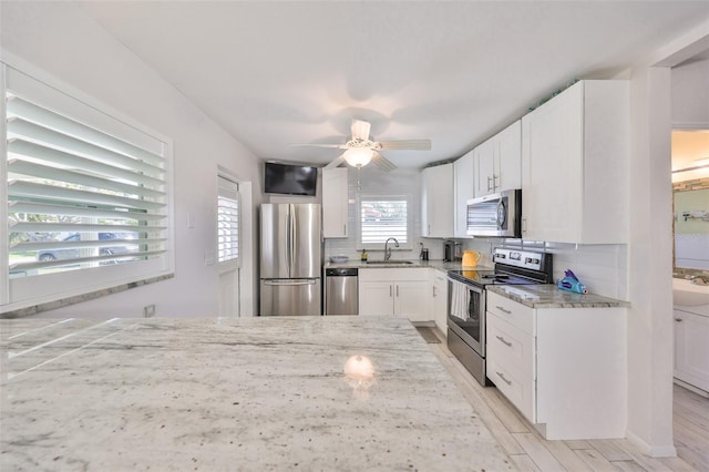 kitchen featuring stainless steel appliances, light stone countertops, backsplash, and white cabinetry