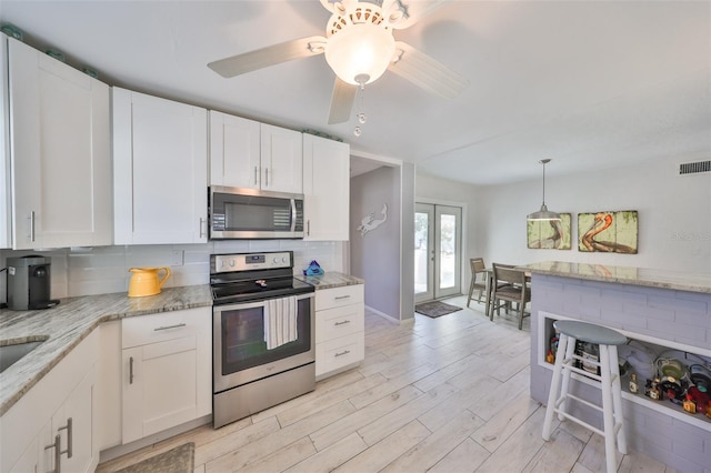 kitchen with light wood-type flooring, visible vents, appliances with stainless steel finishes, white cabinets, and decorative backsplash