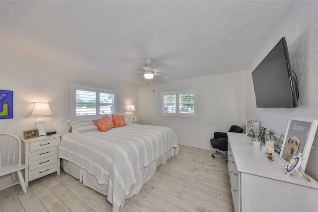 bedroom with multiple windows, light wood-style floors, a ceiling fan, and a textured ceiling