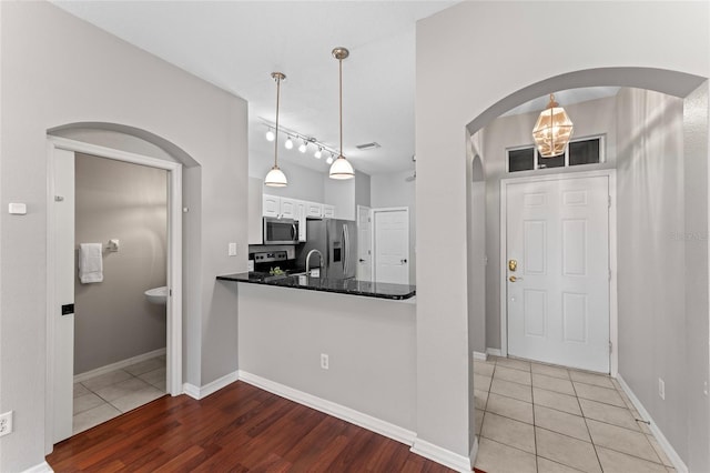 kitchen featuring pendant lighting, stainless steel appliances, arched walkways, white cabinets, and light tile patterned flooring