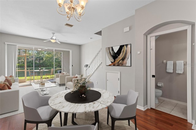 dining space with visible vents, ceiling fan with notable chandelier, wood finished floors, stairway, and baseboards