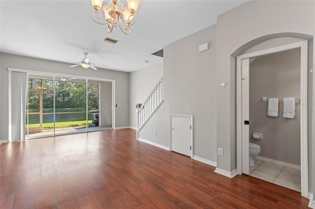 unfurnished living room with visible vents, baseboards, stairs, ceiling fan with notable chandelier, and wood finished floors