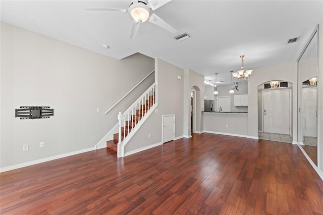 unfurnished living room featuring visible vents, arched walkways, dark wood finished floors, and ceiling fan with notable chandelier