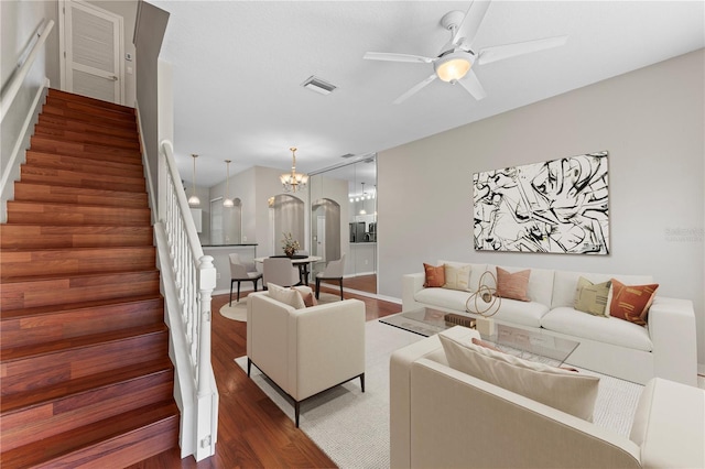 living room with stairway, wood finished floors, visible vents, arched walkways, and ceiling fan with notable chandelier