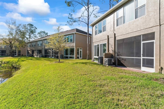 rear view of house with stucco siding, central air condition unit, a lawn, and a sunroom