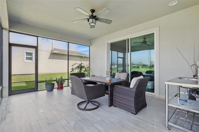 sunroom featuring a ceiling fan, outdoor dining space, and a sink