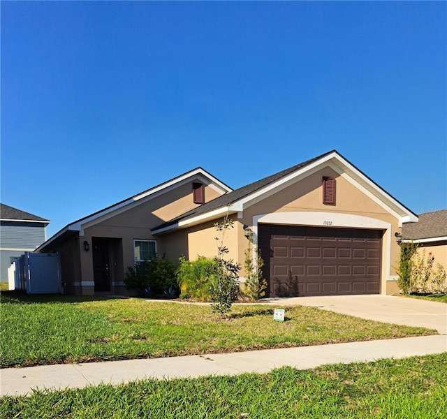 single story home featuring a front lawn, an attached garage, driveway, and stucco siding