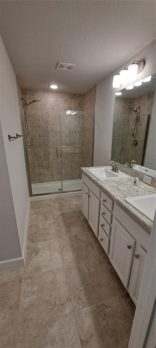 full bath with visible vents, a sink, a shower stall, double vanity, and baseboards