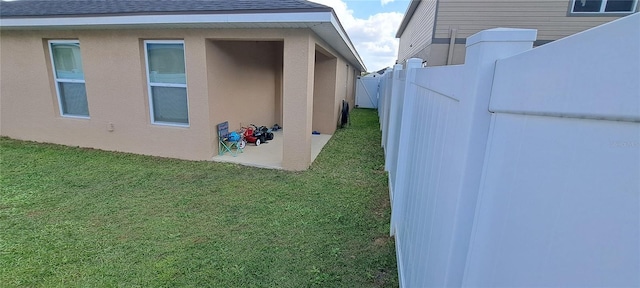 view of property exterior with a yard, fence, roof with shingles, and stucco siding