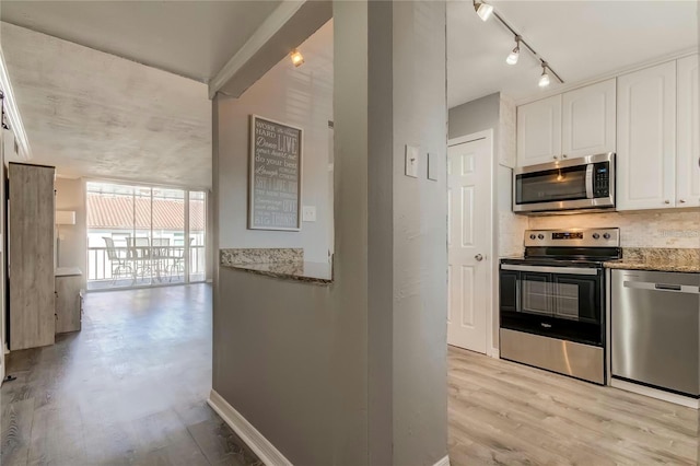 kitchen featuring baseboards, decorative backsplash, appliances with stainless steel finishes, light stone counters, and white cabinetry