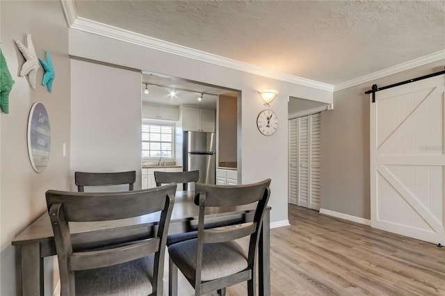 dining area featuring light wood-style floors, a barn door, crown molding, and a textured ceiling