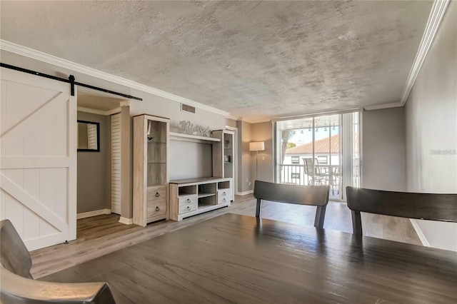 unfurnished room with a textured ceiling, a barn door, wood finished floors, visible vents, and crown molding