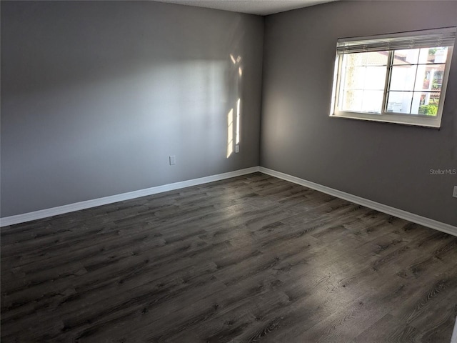 unfurnished room with dark wood-type flooring and baseboards