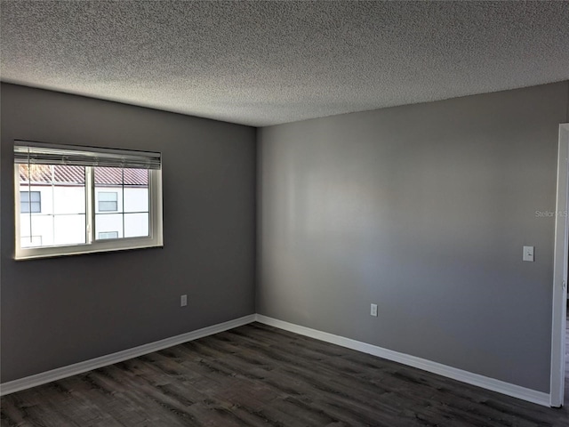 empty room with a textured ceiling, dark wood finished floors, and baseboards