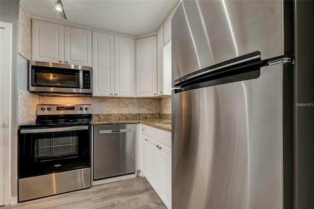 kitchen with light stone counters, stainless steel appliances, backsplash, white cabinets, and light wood-type flooring