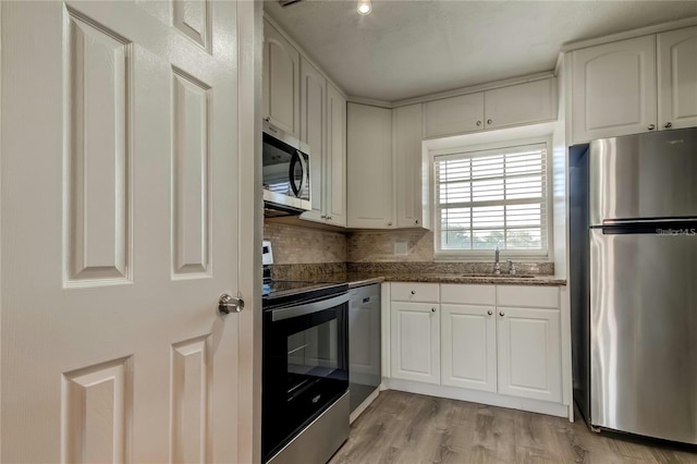 kitchen with light wood finished floors, white cabinets, appliances with stainless steel finishes, a sink, and backsplash