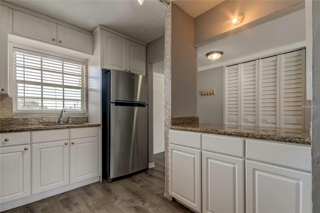 kitchen featuring freestanding refrigerator, a sink, dark stone countertops, and wood finished floors