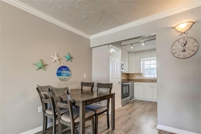 dining room with baseboards, rail lighting, a textured ceiling, crown molding, and light wood-style floors