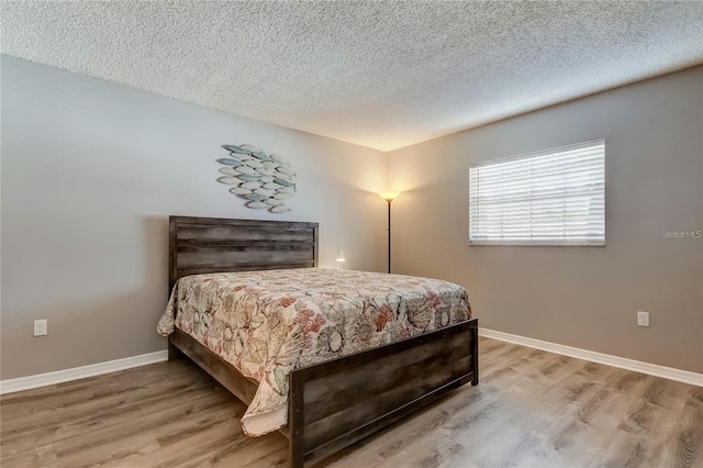 bedroom featuring a textured ceiling, baseboards, and wood finished floors