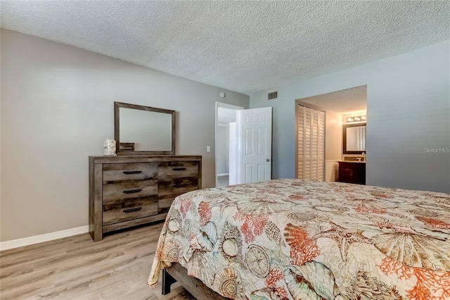 bedroom with a textured ceiling, baseboards, ensuite bath, and light wood-style floors