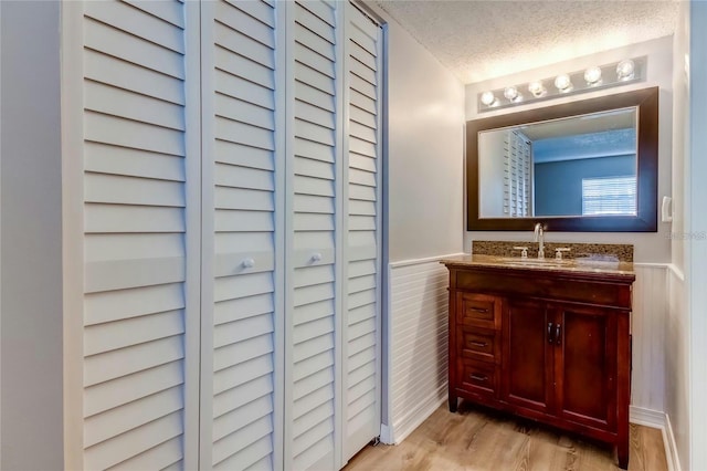 bathroom featuring vanity, wood finished floors, a textured ceiling, and wainscoting