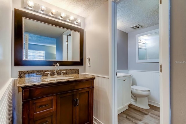 bathroom with a textured ceiling, toilet, a wainscoted wall, vanity, and visible vents