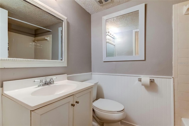 bathroom featuring a shower, a wainscoted wall, visible vents, toilet, and a textured ceiling