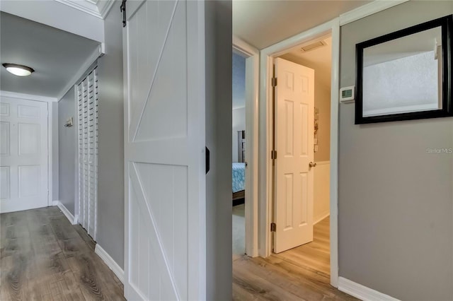 hall featuring baseboards, a barn door, visible vents, and wood finished floors