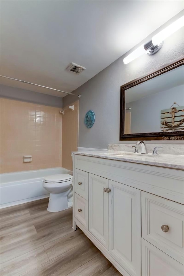 bathroom with toilet, wood finished floors, vanity, visible vents, and tub / shower combination