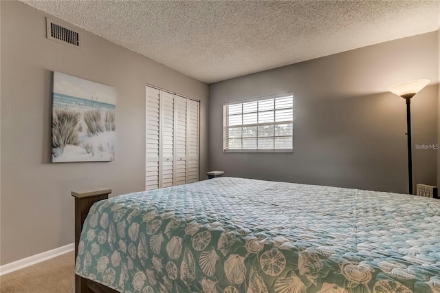 bedroom with a closet, visible vents, carpet flooring, a textured ceiling, and baseboards