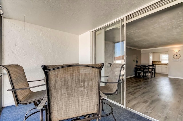 unfurnished dining area with baseboards, a textured wall, ornamental molding, wood finished floors, and a textured ceiling