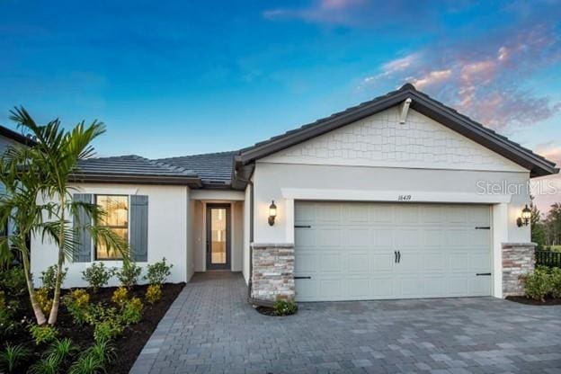 ranch-style house featuring a garage, stone siding, decorative driveway, and stucco siding