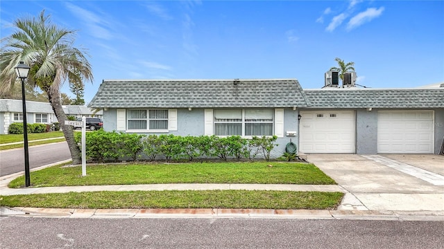 view of front facade featuring stucco siding, mansard roof, concrete driveway, and roof with shingles