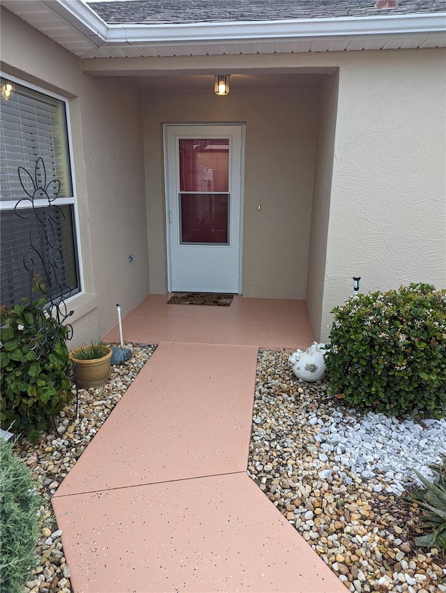 entrance to property featuring stucco siding and a shingled roof