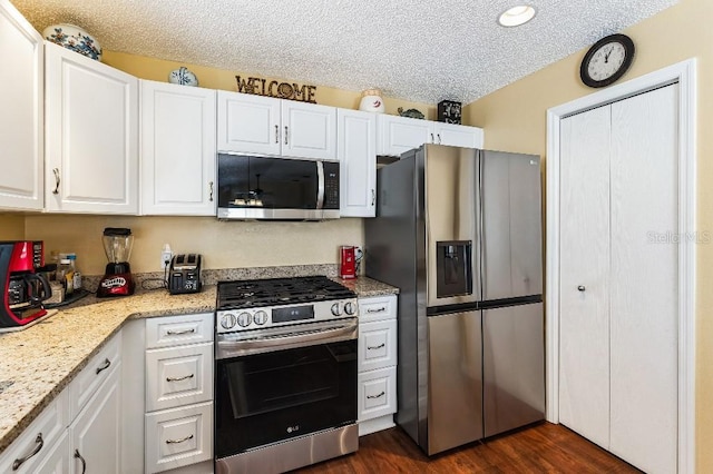 kitchen featuring light stone countertops, dark wood-style floors, white cabinets, appliances with stainless steel finishes, and a textured ceiling