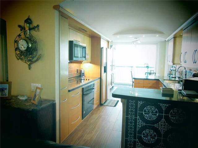 kitchen with tasteful backsplash, a sink, light wood-type flooring, a peninsula, and black appliances