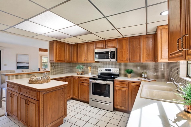 kitchen featuring light countertops, appliances with stainless steel finishes, a sink, and brown cabinets