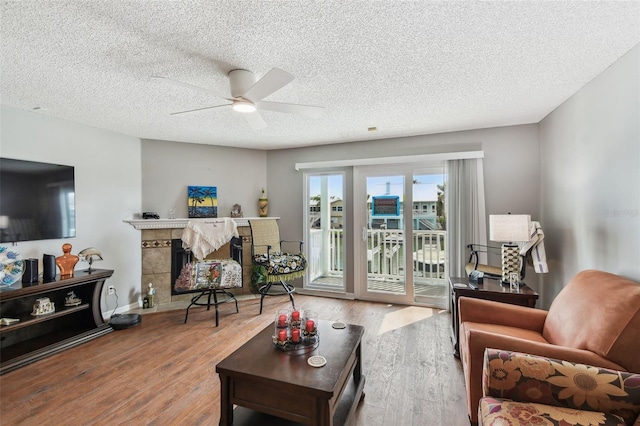 living room with a tiled fireplace, ceiling fan, a textured ceiling, wood finished floors, and baseboards