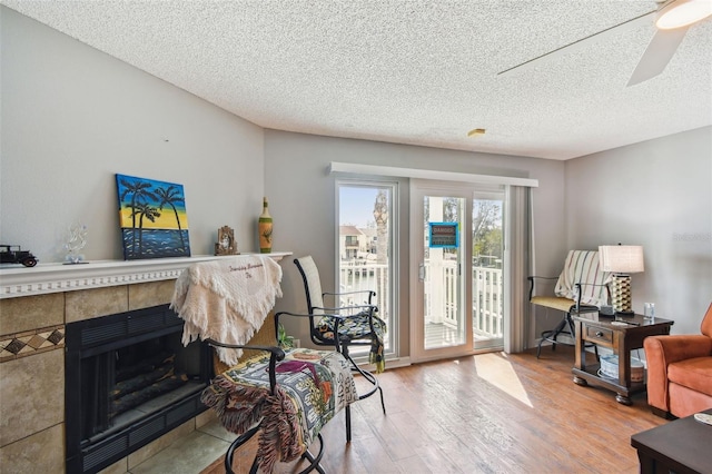 interior space featuring ceiling fan, a textured ceiling, a tiled fireplace, and wood finished floors