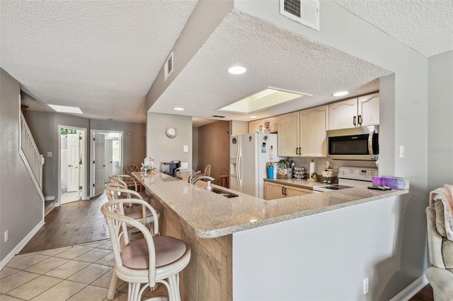 kitchen with light stone counters, visible vents, a sink, white appliances, and a peninsula